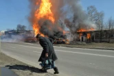 Un habitant passe à proximité d'un véhicule et d'un bâtiment en feu après un tir d'artillerie russe, le 25 mars 2022 à Kharkiv