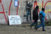 Des réfugiés passent devant un graffiti de l'artiste de rue Banksy représentant en migrant le fondateur d'Apple, Steve Jobs, à l'époque de l'évacuation complète du camp de la "Jungle" de Calais, à Calais, le 24 octobre 2016