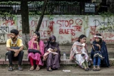 Des étudiants assis devant un mur couvert de graffitis dénonçant les violences politiques et policières, le 11 août 2024 à Dacca au Bangladesh