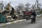 Un homme à moto passe à côté d'un bâtiment détruit dans le village de Moschchun, au nord-ouest de Kiev, le 20 avril 2022