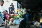 Une femme vend des légumes tandis que sa fille dort à l'arrière sur un carton le 2 mars 2021 à Panama City