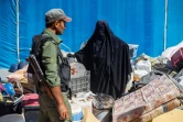 Un membre des forces de sécurité kurdes surveille une femme qui s'apprête à quitter le camp d'al-Hol  qui accueille des proches de combattants présumés du groupe État islamique (EI), le 3 septembre 2023 dans le nord-est de la Syrie