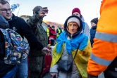 Des réfugiés, dont une femme portant 
un drapeau ukrainien, s'apprêtent à monter dans un bus à destination de la frontière entre l'Ukraine et la Pologne le 18 mars 2022 à Medyka (Pologne)