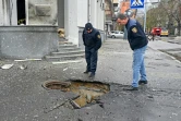 Des membres des services de secours ukrainiens examinent le  cratère formé sur un trottoir après des bombardements dans le centre de la ville ukrainienne de Kharkiv, le 17 avril 2022 