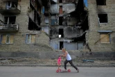 Une enfant en trottinette passe devant un immeuble détruit par des bombardements, le 4 juin 2022 à Gorenka, près de Kiev, en Ukraine