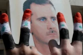 Deux hommes avec les doigts peints dans les couleurs du drapeau syrien font le V de la victoire devant une affiche du président Bachar a-Assad dans le  centre de Damas, le 29 mars 2011