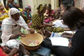 Sur des chaises ou à même le sol avec des nourrissons dans les bras pour certaines, à tour de rôle, les femmes plongent leurs billets d'argent dans une calebasse, le 9 mars 2017 à Grand-Mbao, à la périphérie de Dakar