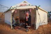 Une Palestinienne prépare à manger à côté d'enfants assis dans une tente de déplacés, avant le repas de rupture du jeûne pendant le mois  musulman du ramadan, dans le camp de Bureij, dans le centre de la bande de Gaza, le 5 mars 2025