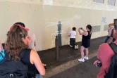 Des passants prennent des photos pendant que la peintre en décor du patrimoine, Agnès Perrone, répare une œuvre d'art de l'artiste de rue Banksy représentant un phare sur la façade d'un bâtiment, après qu'elle a été vandalisée pendant la nuit à Marseille, le 1er juin 2025
