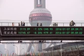 Des gens marchent sur un pont avec un écran montrant les cotations boursières à Shanghai le 7 janvier 2016