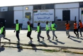 Des migrants camerounais (orange) et Sénégalais (jaune) rejoignent le terrain où ils s'apprêtent à disputer un match de football au camp de Tarjoura en Libye, le 28 février 2018
