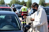 Un prêtre portant un masque de protection dépose une hostie dans la main d'un automobiliste garé sur un parking pour assister à une messe en plein air célébrée par Mgr François Touvet, l'évêque de Châlons-en-Champagne, le 17 mai 2020