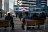 Des Nord-Corénes, assis sur un banc dans une rue de Pyongyang le 1er mars 2019, regardent sur un écran géant la speakrine officielle donner des informations sur la rencontre entre le président américain Donald Trump et leur leader Kim Jong Un à Hanoï