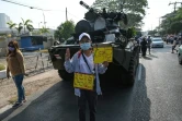 Un manifestant brandit des pancartes pro-démocratie près de véhicules blindés de l'armée à Rangoun, le 15 février 2021