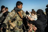 Un combattant des Forces démocratiques syriennes oriente une femme portant un bébé et qui attend d'être fouillée après avoir quitté le dernier réduit du groupe Etat islamique à Baghouz, dans l'est de la Syrie, le 1er mars 2019 