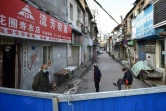 Des habitants derrière une barrière bloquant l'entrée dans leur quartier à Wuhan, la ville du centre de la Chine où est apparue l'épidémie de coronavirus, le 23 février 2020