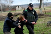 Une femme soutenue par des policiers lors de l'exhumation du corps de son mari tué à Andriïvka, près de Kiev, le 11 avril 2022 en Ukraine