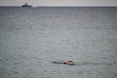 Un homme nage dans la mer Méditerranée alors qu'un navire de guerre croise au large de la ville côtière de Nahariya, en Israël, le 3 janvier 2024