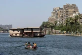 Une famille de pêcheurs  assise dans un bateau face à une péniche amarrée sur l'une des rives du Nil entre le quartier Zamalek et le quartier Agouza le 27 juin 2022