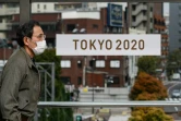 Un passant masqué devant une banderole pour les Jeux olympiques 2020 de Tokyo le 27 mars 2020 à Tokyo