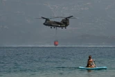 Un vacancier pratiquant le stand up paddle (planche à rame) observe un hélicoptère se ravitailler en eau près de la plage de Lambiri à Patras (Grèce) le 1er août 2021