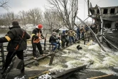 Des membres de la défense civile ukrainienne font passer des armes de l'autre côté d'un pont bombardé sur le front au nord de Kiev, le 1er mars 2022