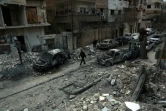Photo prise le 25 février 2018 montrant un homme marchant dans une rue de la ville de Douma au milieu de voitures détruites et immeubles endommagés après des raids aériens du régime syrien sur la Ghouta orientale, une enclave rebelle près de Damas bombardée par le régime syrien