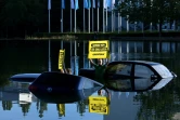 Un militant de l'ONG Greenpeace brandit une pancarte "rétrécissez maintenant ou vous coulerez bientôt", faisant allusion à la taille des automobiles et à leurs émissions de CO2, près de vieilles voitures que des militants ont partiellement immergées dans un plan d'eau proche de l'entrée du salon de l'automobile de Munich le 4 septembre 2023