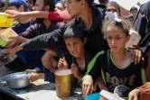 Des enfants palestiniens font la queue pour obtenir un repas chaud lors d'une distribution assurée par une cuisine soldiaire au camp de réfugiés de Nousseriat, dans le centre de la bande de Gaza, le 5 mai 2025