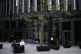 De rares employés de bureaux sont assis à l'extérieur d'un immeuble dans les rues désertées de la City à Londres, pendant l'épidémie de coronavirus le 6 août 2020