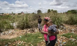 HélÚne Mvubu porte sa fille en marchant dans un champ pollué à Lubumbashi en République démocratique du Congo le 24 novembre 2025 ( AFP / Glody MURHABAZI )