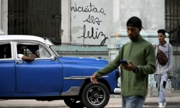 Des Cubains marchent devant le graffiti "Necesitas ser feliz" (Tu dois être heureux) du graffeur cubain Mr. Sad, à La Havane, le 12 décembre 2024 ( AFP / YAMIL LAGE )