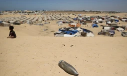 Un obus non explosé non loin d'un enfant assis sur le sable près d'un camp de fortune pour Palestiniens déplacés dans la zone de Tel al-Sultan à Rafah, dans le sud de la bande de Gaza, le 30 mai 2024 ( AFP / Eyad BABA )