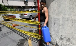 Un homme masqué, un bidon d'eau à la main, franchit la limite d'une rue confinée pour cause de Covid-19 à Manille, le 10 mars 2021
