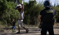 Un habitant, transportant sur sa tête des sacs de provisions, passe avec des enfants, devant un gendarme à un barrage routier à Saint-Louis, au sud de Nouméa, le 23 septembre 2024 en Nouvelle-Calédonie ( AFP / SEBASTIEN BOZON )