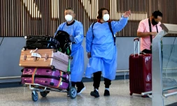 Des passagers vĂȘtus de blouses de protection Ă leur arrivĂ©e Ă l'aĂ©roport de Melbourne le 29 novembre 2021