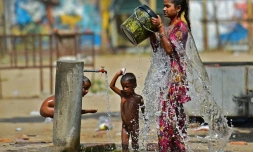 Une femme et des enfants se rafraichissent avec l'eau d'un robinet public lors d'une chaude journée d'été, le 28 avril 2022 à Allahabad, en Inde