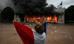 Un protestataire enveloppé dans un drapeau français devant l'antenne de l'Office du tourisme de Lyon en feu, lors d'une manifestation contre la vie chère, le 17 octobre 2026 ( AFP / Jeff PACHOUD )