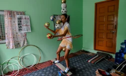 Han Myint Mo tient en équilibre une balle dorée sur la lame d'un couteau, le manche entre ses dents, lors d'un entraînement de jonglage, le 5 juillet 2022 à Rangoun, en Birmanie