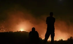 Deux personnes regardent des incendies près du village de Malona sur l'île touristique grecque de Rhodes, le 23 juillet 2023 ( AFP / SPYROS BAKALIS )