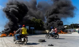 Des motos passent devant des pneus en feu après une manifestation de policiers consécutive à une attaque de gang sur un commissariat, à Port-au-Prince, le 26 janvier 2023