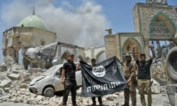 Un membre du Service du contre-terrorisme (CTS) irakien lève les bras en signe de victoire tandis que d'autres tiennent le drapeau de l'Etat islamique devant la mosquée al-Nouri de Mossoul, le 30 juin 2017