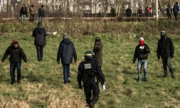 Un policier face à des migrants qui essaient de monter dans des camions sur l'A16 à Coquelles près de Calais le 21 janvier 2016