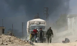 Un combattant des prorégime marche au côté de civils sortant de la localité de Hammouriyé dans l'enclave rebelle de la Ghouta orientale, cible d'une offensive du régime syrien, le 16 mars 2018