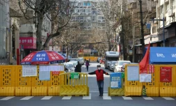 Un homme devant une barrière empêchant l'enrée dans un quartier confiné de Wuhan, le 15 mars 2020 pendant l'épidémie du nouveau coronavirus