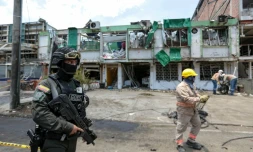 Un membre du Groupe des opérations spéciales de la police nationale colombienne monte la garde tandis que des agents de nettoyage déblayent les débris du site d'une explosion à la bombe survenue la veille à Cali, en Colombie, le 22 août 2025