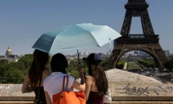 Des touristes se protègent du soleil sous un paraplluie devant la Tour Eiffel lors d'une vague de chaleur à Paris, le 27 mai 2026