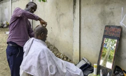 Papy Kalume, un coiffeur de rue, coupe les cheveux d'un client sur le trottoir à Kinshasa, le 17 octobre 2024 en RDC