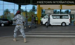 Des agents de sécurité escortent des migrants vers un centre de l'Agence nationale de santé publique (NPHA) aprÚs leur arrivée à l'aéroport international de Freetown, le 20 mai 2026 à Lungi, en Sierra Leone