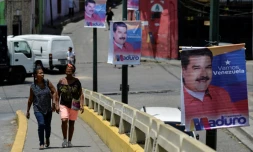 Des femmes marchent près d'une affiche de campagne du président vénézuélien Nicolas Maduro, dans les rues de Caracas, le 11 mai 2018